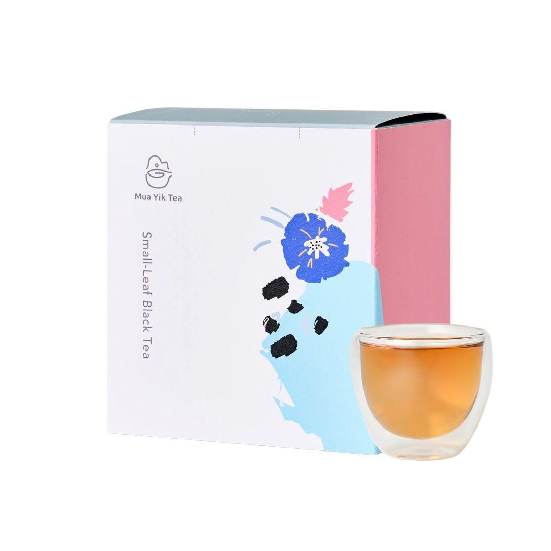 Mia Vlk Tea Small Leaf Black Tea packaging box with a pink side panel and blue floral illustration, shown next to a clear double-walled glass cup filled with amber-black tea on a white background.