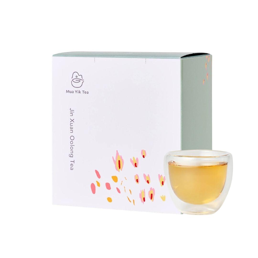 Mua Yik Tea Jin Xun Oolong Tea packaging box in white with pink and orange floral accents, shown next to a clear glass cup filled with amber tea, on a white background.