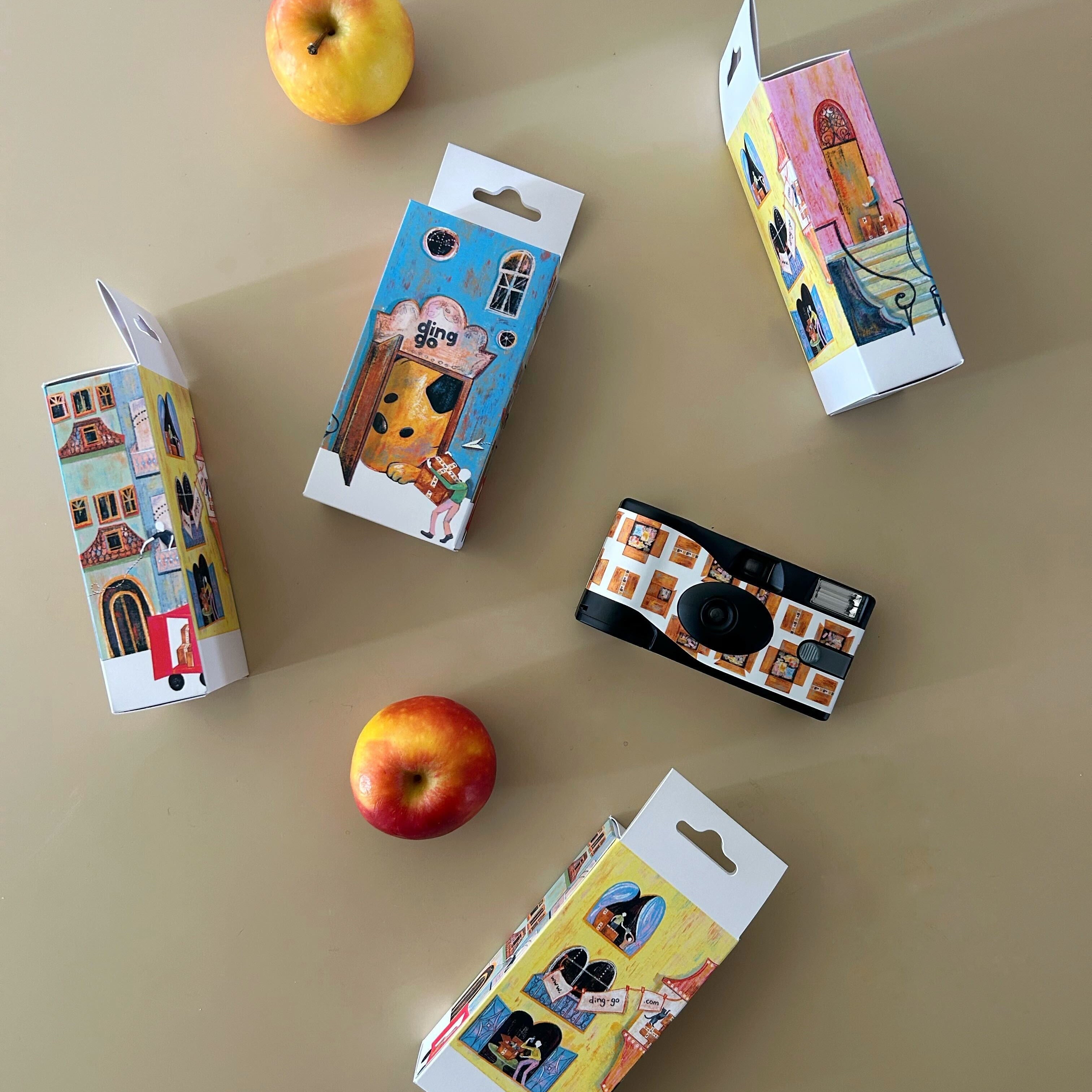 Small camera and its packaging on a beige surface with apples.